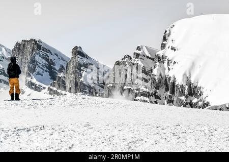 Mann mit Rucksack und gelber Trekkinghose, der vor einer verschneiten Berglandschaft in der Schweiz steht. Churfirsten, Chäserrugg Stockfoto