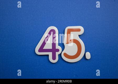 Die Nummer 45, auf blauem Hintergrund, von oben fotografiert, lila und orange. Stockfoto