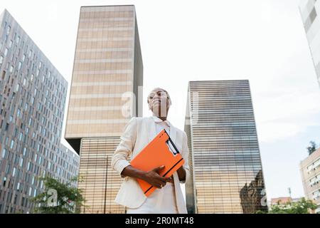 Befähigte afrikanische Geschäftsfrau mit Orange Folder im städtischen Geschäftsbezirk Stockfoto