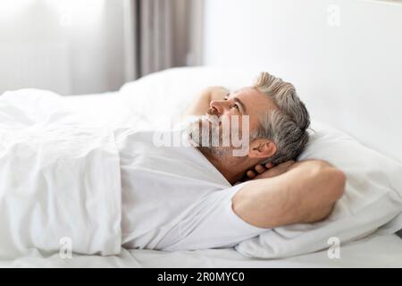 Seitenansicht eines glücklichen erwachsenen Mannes, der im Bett lächelt Stockfoto