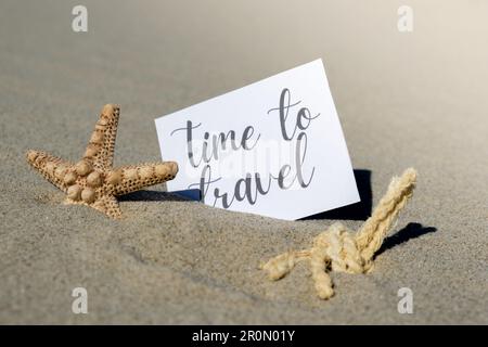 ZEIT FÜR REISEN Text auf Papiergrußkarte auf Hintergrund der Seesterne Muschel Sommerurlaub Dekor. Sandstrand, Sonnenküste. Postkarte zum Urlaubskonzept. Geschäftskonzept „Getting Away Travel“ Stockfoto