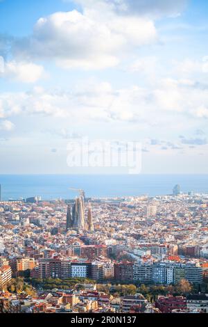 Aus der Vogelperspektive sehen Sie die wunderschöne Stadt mit Wohngebäuden und der hohen Kirche Sagrada Familia im sonnigen Barcelona vor dem endlosen blauen Meer Stockfoto