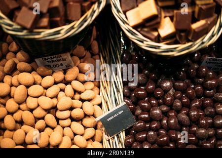 Draufsicht auf verschiedene Haufen glasierter Erdnüsse in Korbkörben mit glutenfreier Inschrift auf dem lokalen Markt in Barcelona Stockfoto