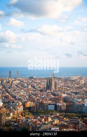 Aus der Vogelperspektive sehen Sie die wunderschöne Stadt mit Wohngebäuden und der hohen Kirche Sagrada Familia im sonnigen Barcelona vor dem endlosen blauen Meer Stockfoto