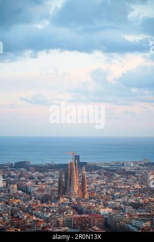 Aus der Vogelperspektive sehen Sie die wunderschöne Stadt mit Wohngebäuden und der hohen Kirche Sagrada Familia im sonnigen Barcelona vor dem endlosen blauen Meer Stockfoto