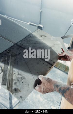 Anonym tätowierter männlicher Meister mit spezieller Ausrüstung zur Messung des Surfbretts bei der Grössenprüfung während der Arbeit in einer Fachwerkstatt Stockfoto