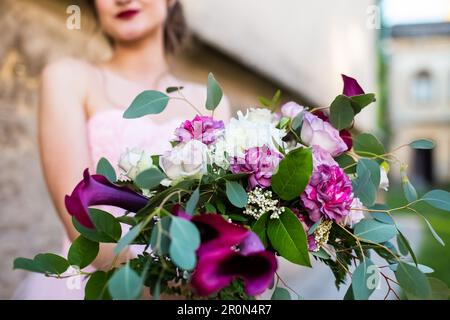 Hochzeitsstrauß in den Händen der Braut, Nahaufnahme, leuchtend rote Calla-Lilien-Blumen. Glückliche junge Braut mit ihrem Brautstrauß. Schließen Stockfoto