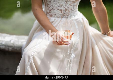 Die Braut hält ein Glas Champagner in der Hand und trägt ein wunderschönes Hochzeitskleid. Hochzeitstag Stockfoto