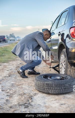 Ein Latino-Mann im Anzug wechselt einen Platten Reifen seines Autos am Straßenrand. Stockfoto