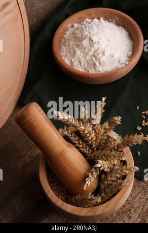 Mörtel mit Spikes und Schüssel Weizenmehl auf einem Holztisch Stockfoto