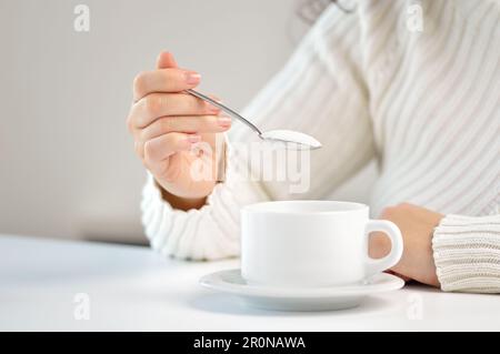 Die Hand einer Frau, die Zucker mit einem Löffel in den Kaffee schüttet Stockfoto