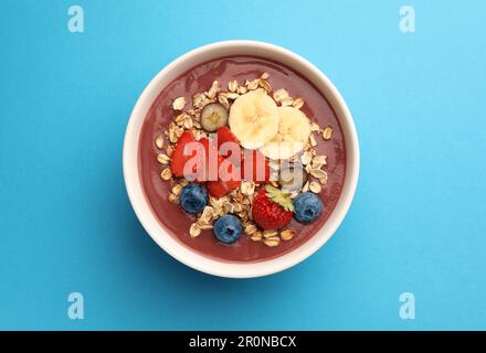 Köstliche Smoothie-Schüssel mit frischen Beeren, Banane und Müsli auf hellblauem Hintergrund, Draufsicht Stockfoto