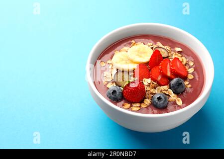 Köstliche Smoothie-Schüssel mit frischen Beeren, Banane und Müsli auf hellblauem Hintergrund. Platz für Text Stockfoto