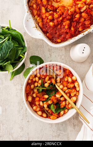 Gesundes Frühstück und Mittagessen, gedünstete weiße Bohnen mit Karotten, Zwiebeln und Tomaten mit Spinatblättern, eine Schüssel Bohnen und Spinat Stockfoto