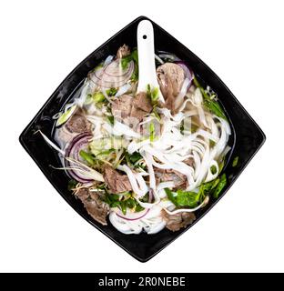 vietnamesische Suppe Pho Bo mit Reisnudeln, Brühe, Zwiebeln, Gemüse, Rindfleisch in der Schüssel mit Ausschnitt aus Keramiklöffel auf weißem Hintergrund Stockfoto