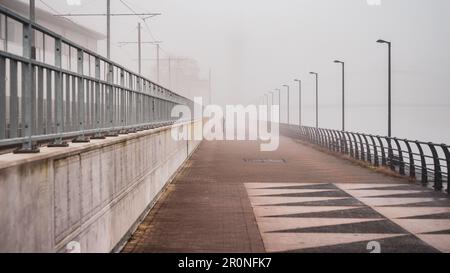 Breite Aufnahme einer Silhouette, die einen Pfad entlang geht, umgeben von Nebel/Nebel in einer städtischen Betonumgebung Stockfoto