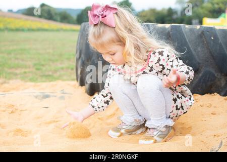 Ein blondes, kleines, kaukasisches Kleinkind, das im Sand spielt. Sensorisches Spiel Stockfoto