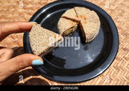 Weiblich mit Scheiben Anjeer-Kuchen, süßes indisches Gericht bedeckt mit Mohnsamen. Feigendessert mit Datteln, Mandeln und Pista Stockfoto