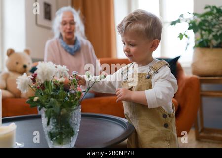 Ein kleiner Junge, der Blumen in einer Vase ansieht. Stockfoto