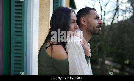 Freundin umarmte Freund von hinten, während sie draußen auf dem Balkon stand. Ein liebenswertes Paar aus dem Nahen Osten, das Liebe und Unterstützung zeigt, während conte Stockfoto