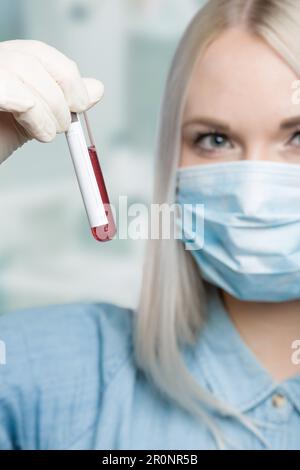 Eine Wissenschaftlerin behandelt ein Blutteströhrchen vor einem Laborraum Stockfoto