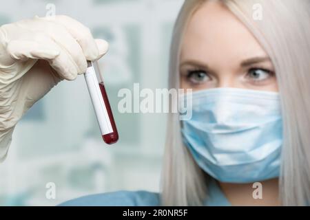 Eine Wissenschaftlerin behandelt ein Blutteströhrchen vor einem Laborraum Stockfoto