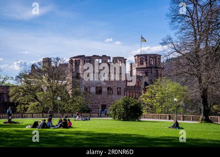 Menschen, die auf dem Gras im Heidelberger Schlossgarten in der Nähe der Burgruinen in Heidelberg sitzen Stockfoto