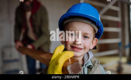 Vater und sein kleiner Sohn arbeiten vor ihrem unvollendeten Haus, tragen hölzerne Panicle. Stockfoto