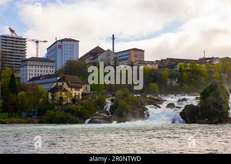 Rheinfälle und Schweizer Flagge mit Industriebau in Neuhausen in Schaffhausen, Schweiz. Stockfoto