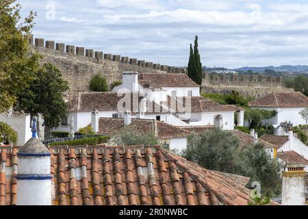 Panoramablick über die orangefarbenen Ziegeldächer von Obidos, Portugal mit typischer mittelalterlicher Architektur und die Mauern der Burg von Obidos im Hintergrund Stockfoto