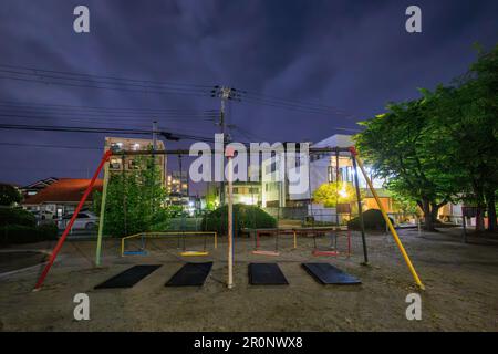 Leere Schaukeln auf dem Kinderspielplatz im ruhigen Park in der Nachbarschaft bei Nacht Stockfoto