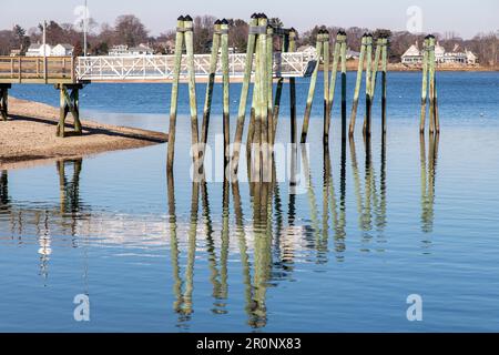 Blick über das Wasser von Greenwich Cove mit einem Pier und einer langen Reihe von Anlegemasten hoch über dem Ebbe Wasser von Tod's Point, Greenwich, CT, Stockfoto