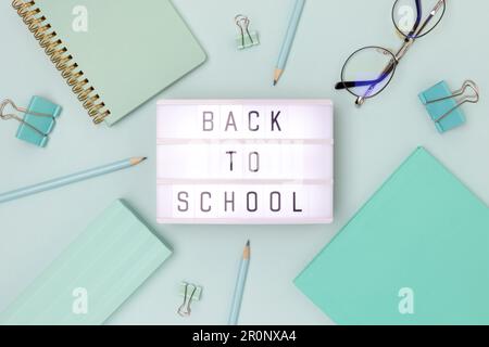 Zurück in die Schule. Lichtbox mit Buchstaben und Rahmen aus Schreibwaren auf blauem Hintergrund. Stockfoto