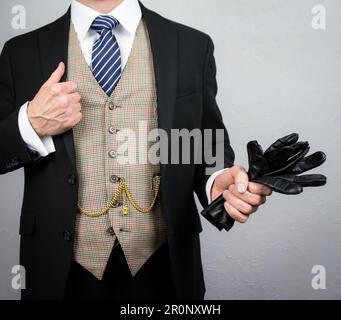 Porträt von eleganten Lederhandschuhen mit Männeranzug in sorgenfreier Haltung. Vintage-Stil und elegante Mode des klassischen britischen Gentleman. Stockfoto