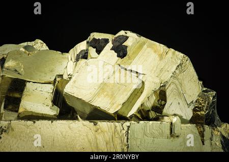 Kubische Pyrit-Kristalle auf schwarzem Hintergrund. Texturhintergrund für Makrodetails. Nahaufnahme von rohem, unpoliertem Halbedelstein Stockfoto