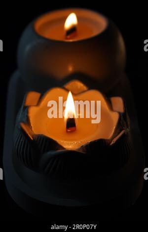 Ein Satz von weißen Kerzen, die im Dunkeln auf schwarzem Hintergrund flackern, wobei eine Kerze im Vordergrund fokussiert ist. Eine Kerze anzünden. Eine brennende Kerze Stockfoto