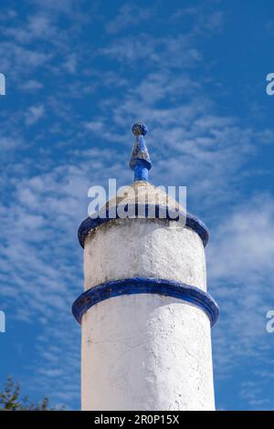 Blick aus dem niedrigen Winkel auf einen kleinen Kirchturm oder Turm in Weiß und Blau in der Stadt Obidos, Portugal, mit kleinen Verzierungen auf der Oberseite vor einem blauen Himmel Stockfoto