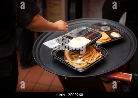 Ein Blick auf einen Mitarbeiter, der sich darauf vorbereitet, mehrere Lebensmittelbehälter für unterwegs in einer Restaurantküche zu verpacken. Stockfoto