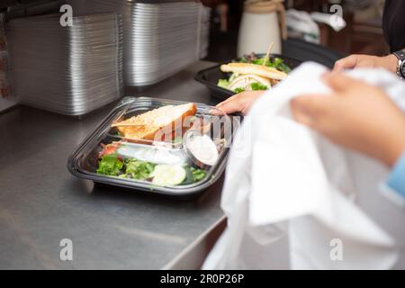 Ein Blick auf einen Mitarbeiter, der sich darauf vorbereitet, einen Lebensmittelbehälter für unterwegs in einer Restaurantküche zu verpacken. Stockfoto