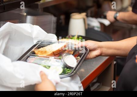 Ein Blick auf einen Mitarbeiter, der sich darauf vorbereitet, einen Lebensmittelbehälter für unterwegs in einer Restaurantküche zu verpacken. Stockfoto