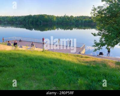 Ein Fischer, der vom Pier aus auf einem See angeln will. Ein Fischer fischt auf dem Fluss, Rückansicht, vom Ufer aus. Sport, Erholung, Lifestyle. Angeln auf der Stockfoto