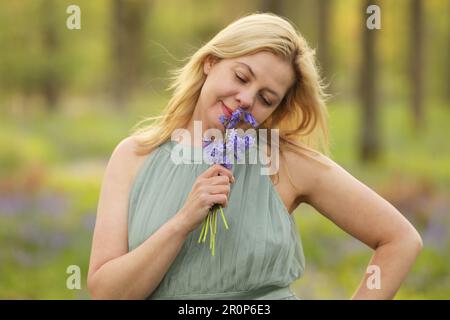 Eine Frau, die ein grünes Kleid trägt und einen Haufen Bluebells in der Hand hat Stockfoto