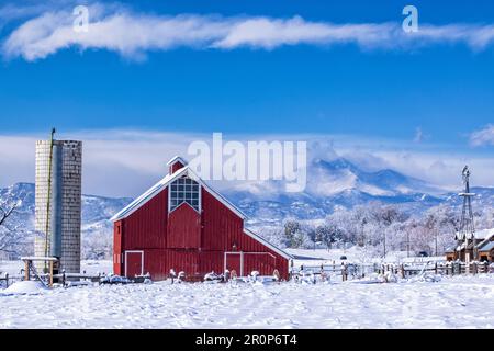 Die leuchtend rote Stroh/Dickens-Scheune und eine Windmühle vom Agricultural Heritage Center in Longmont, Colorado, mit Longs Peak im Hintergrund. Stockfoto