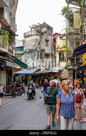 Touristen laufen in einer typischen Straße mit einem zufälligen Stil von Gebäuden in verschiedenen Reparaturzuständen in Hanoi, Vietnam. Stockfoto