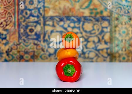 Drei kleine Paprika, eine rote, eine gelbe und eine orangefarbene, übereinander angeordnet. Stockfoto