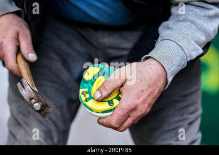 Man Farrier, der Plastik-Hufeisen am HUF installiert. Nahaufnahmen von Händen, die Tierfüße halten, und verschwommenem Hammer Stockfoto