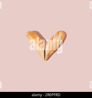 Herz aus frischem französischem Baguette auf pinkfarbenem Hintergrund. Minimales Essenskonzept. Stockfoto