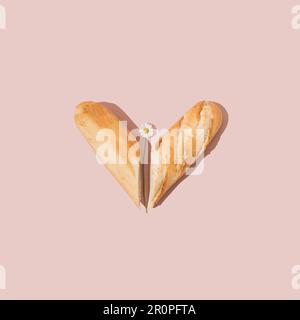 Herz aus frischem französischem Baguette und Gänseblümchen auf pinkfarbenem Hintergrund. Minimales Sommerspeisenkonzept. Stockfoto