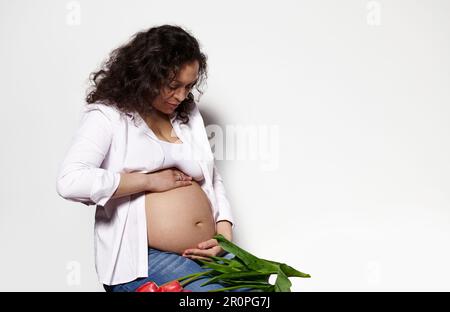 Attraktive schwangere Frau, die den Bauch berührt, isolierter weißer Hintergrund. Körperpositivität Schwangerschaft Mutterschaft erwartet Baby Stockfoto