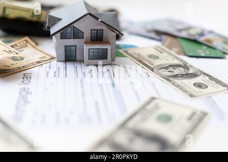 Buchhalter, der an Einkommensteuerformularen oder Budgetplanung mit Währungsnotizen, Taschenrechner und Haus-3D-Modell arbeitet Stockfoto